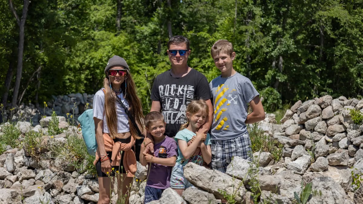 A family of five bonding on a sunny outdoor adventure surrounded by rocks and greenery.